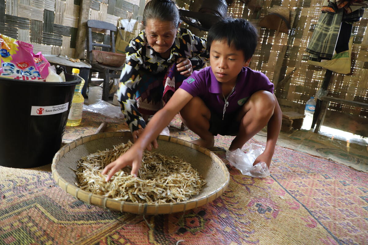 Chan is helping his grandmother storing dried fish given by Save the Children
